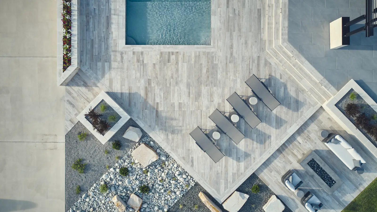 Overhead aerial of a rectangular pool, spa, and porcelain paver deck with chaise lounges