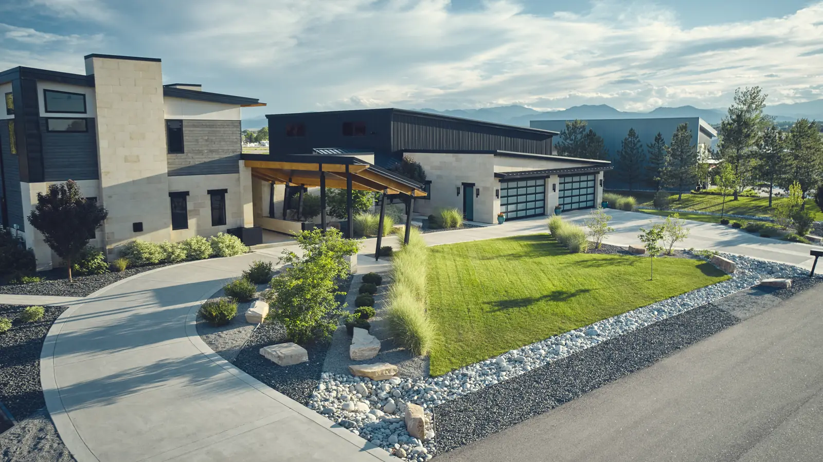 Modern Colorado home with covered outdoor living area, curved driveway, lawn, and boulder landscaping
