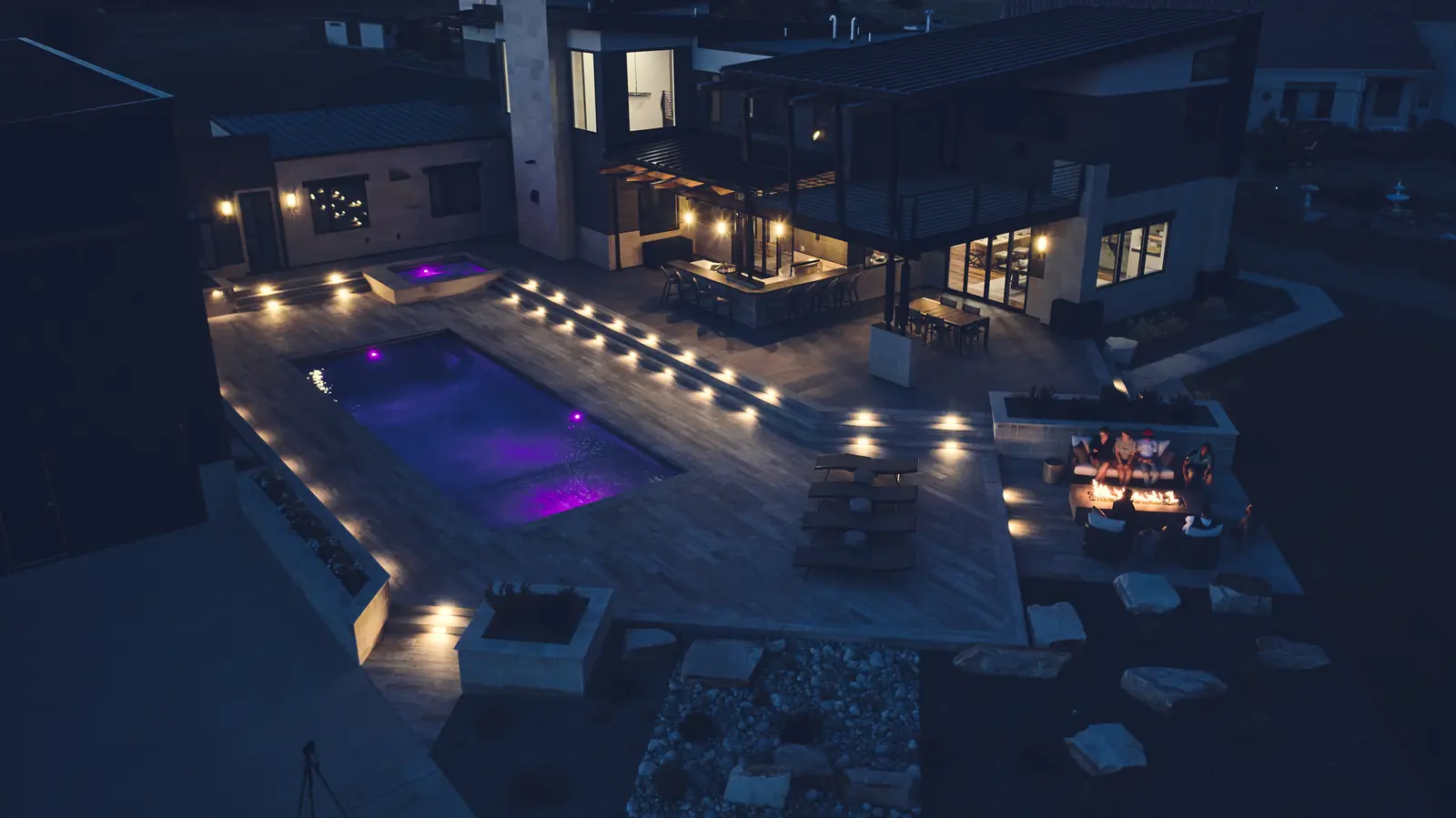Evening view over an LED-lit pool with recessed deck step lights and fire pit seating