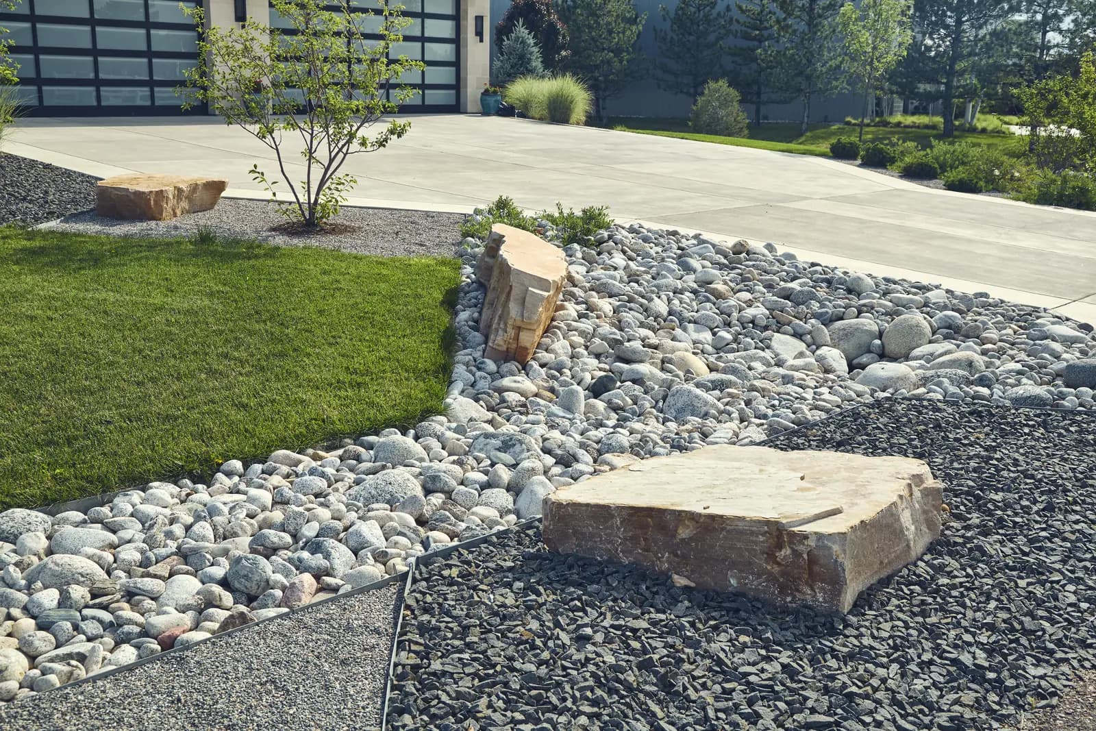 Detail of river rock drainage bed, boulder slab, and steel edging along a concrete drive
