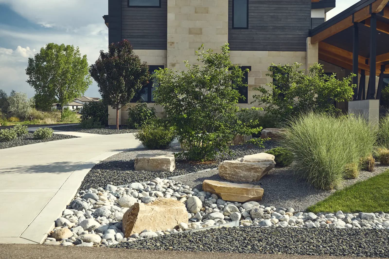 Side yard planting of grasses and boulders in river rock beside the driveway