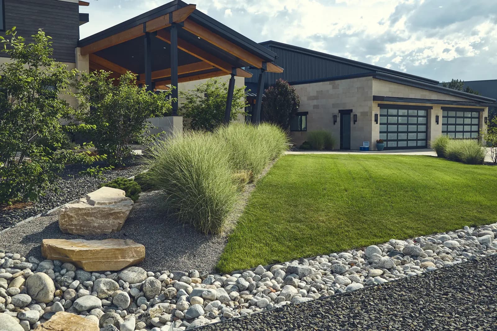 Timber-accented covered entry with lawn, ornamental grasses, and boulder landscape