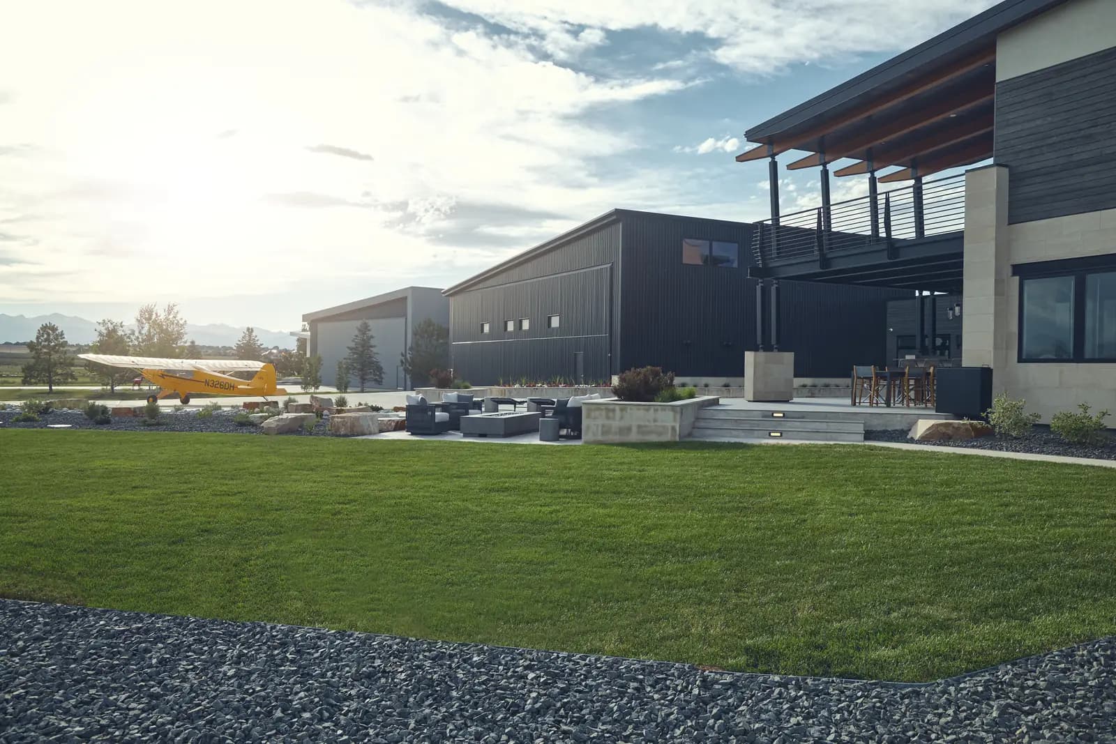 Sunlit lawn between the home and hangar with boulder and gravel landscape
