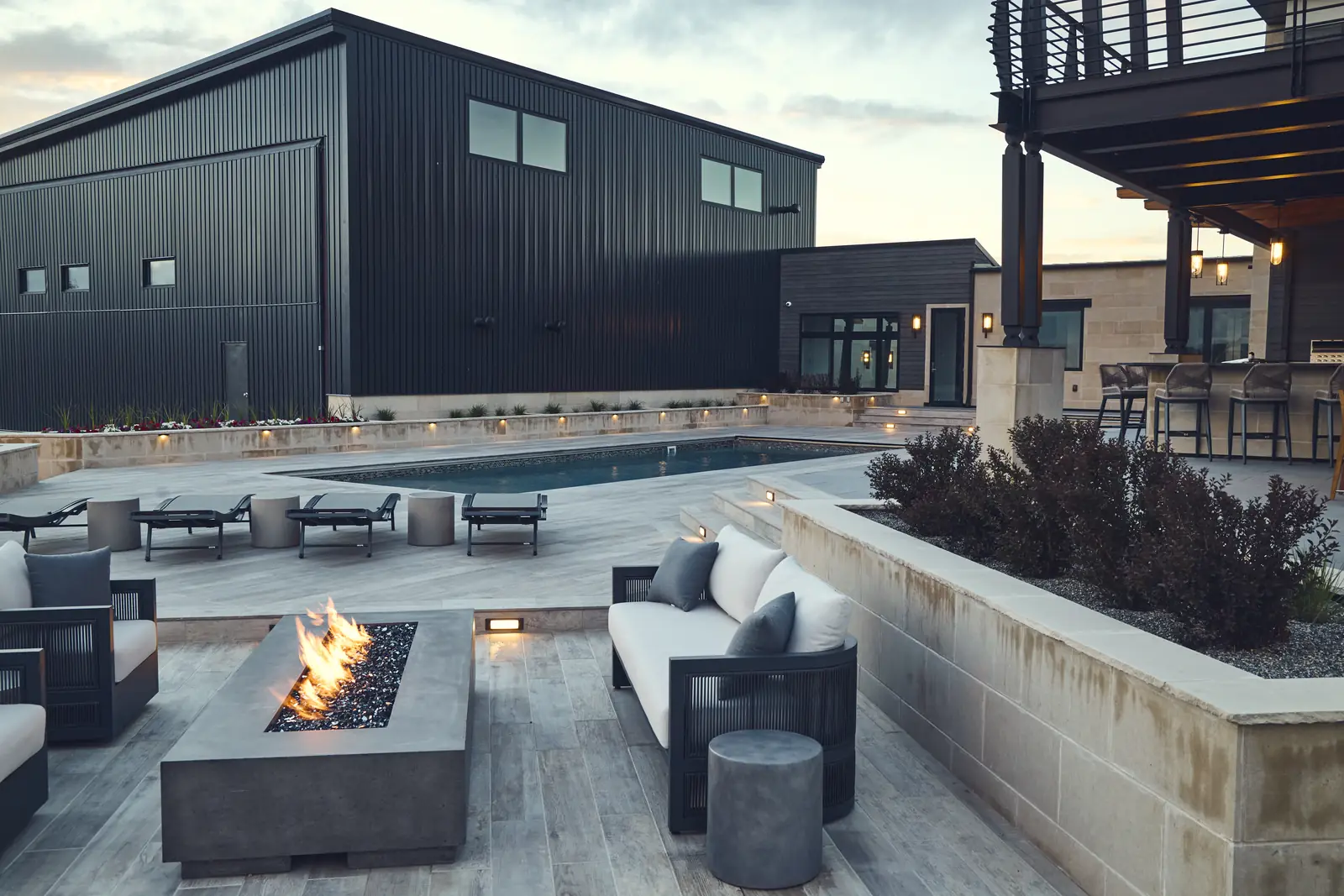 Burning concrete fire pit with outdoor sofas and limestone wall at dusk