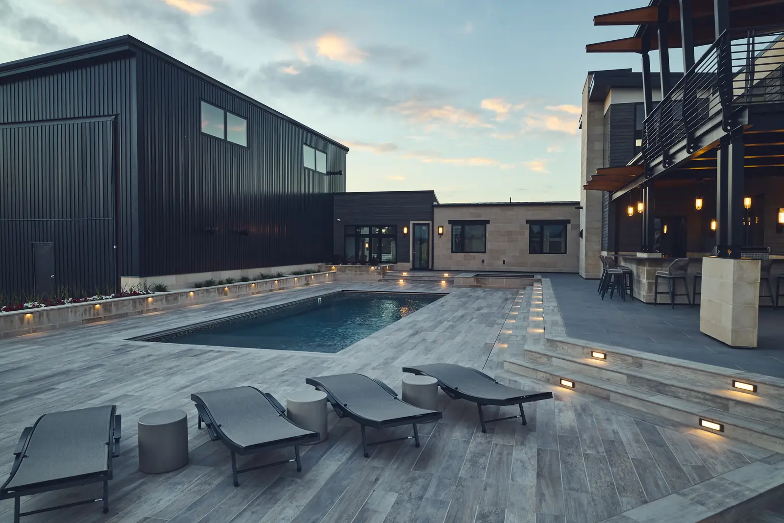 Pool with chaise lounges and recessed step lighting glowing at dusk
