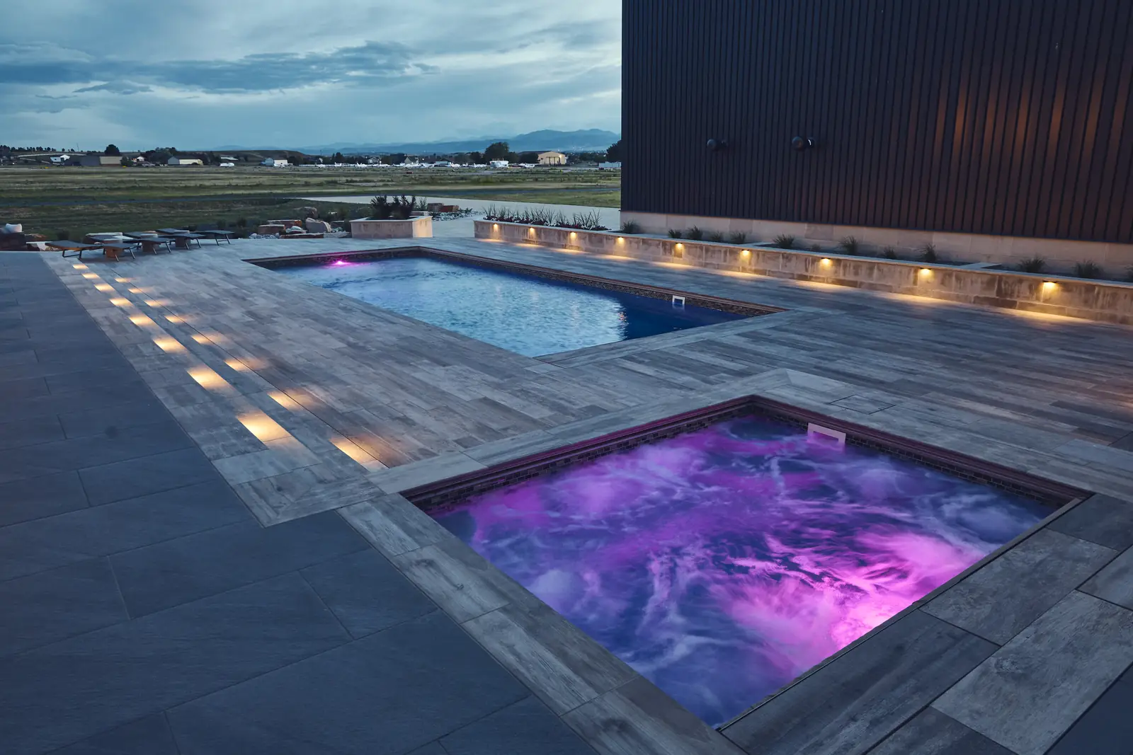 Elevated night view of the pool and purple-lit spa with deck lighting