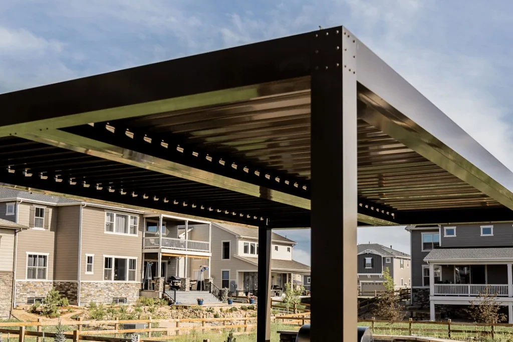 Low-angle detail of powder-coated aluminum louvered roof: structural corner, partially open blades for drainage and light control, suburban Colorado backdrop.
